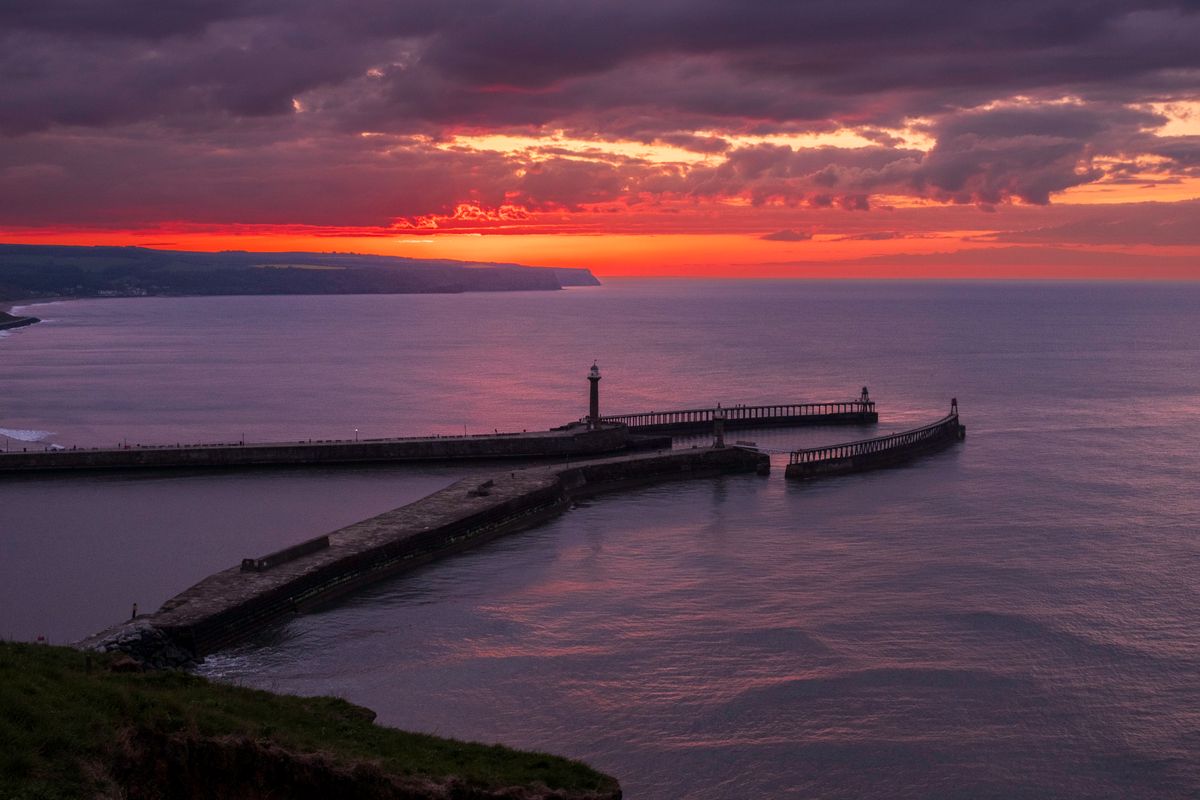 Whitby Harbour at sunset, photographed as the last light burned across the horizon beyond the piers and lighthouse.